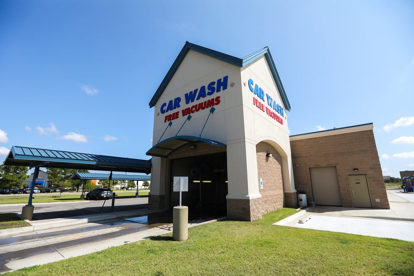 Fast Wash Coweta tunnel entrance under a blue sky, with CAR WASH and FREE VACUUMS lettering on the cream tower and covered vacuum stations to the left