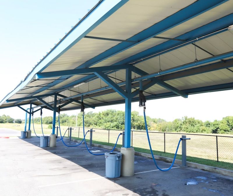 Covered vacuum stations with blue hoses beside the Fast Wash lot